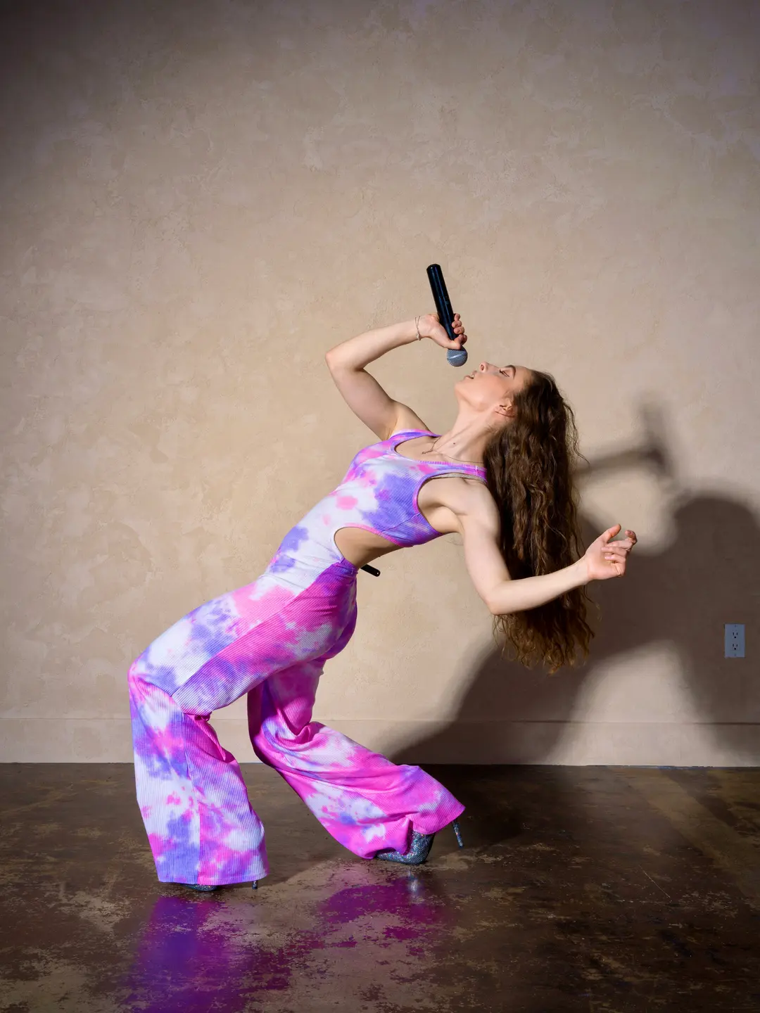 Rebelle leaning back and singing into a microphone in a pink and purple outfit